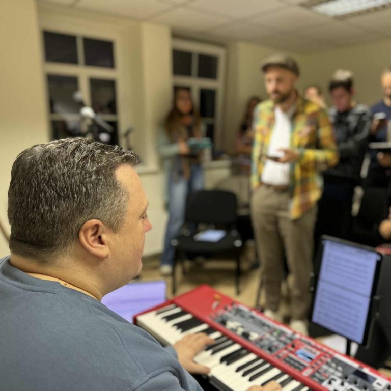 Mann am Keyboard spielt, während eine Gruppe von Menschen im Hintergrund zuschaut.